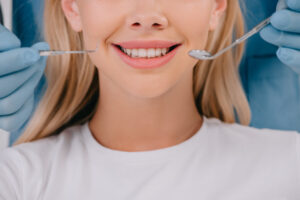 cropped view of dentist holding mouth mirror and dental probe near smiling woman